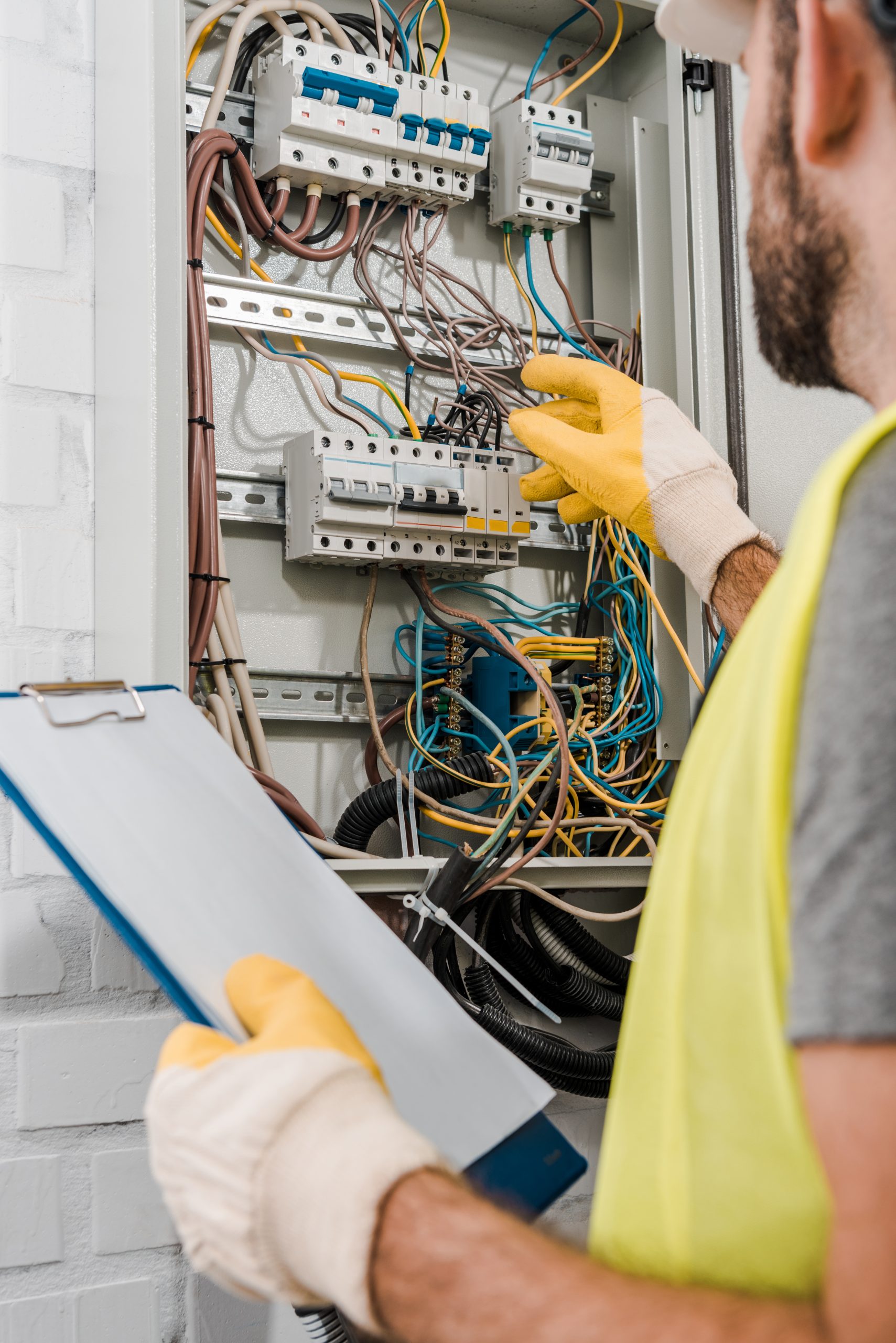 cropped image of electrician holding clipboard and inspecting electrical box in corridor Electrician Bli Bli - electrician working on switchboard
